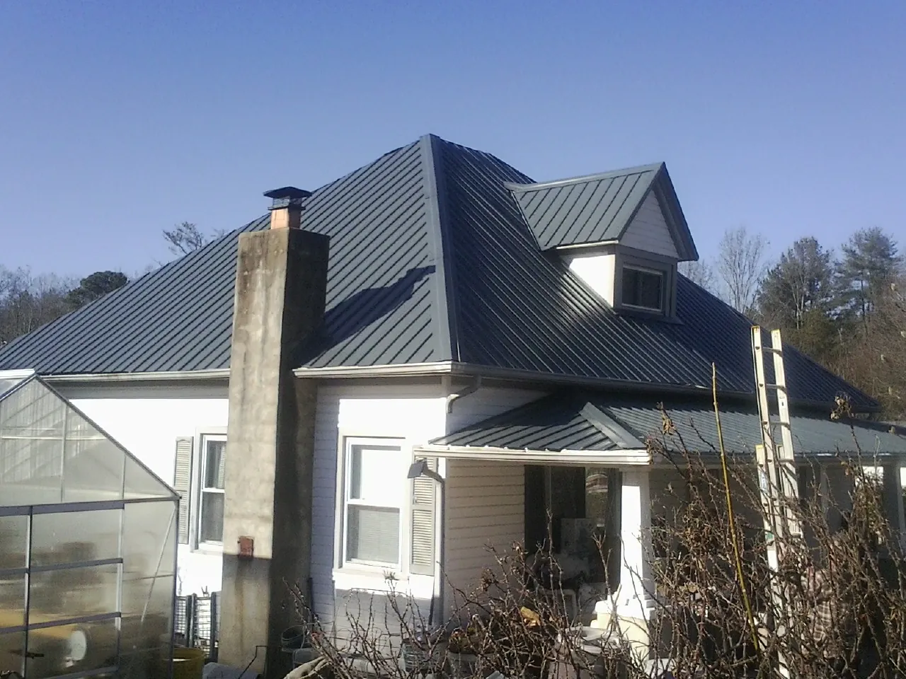 Dark blue standing seam metal roof on a white farmhouse with dormer — Slate & Tile Roof Repair by Roofing Brothers in Brooker