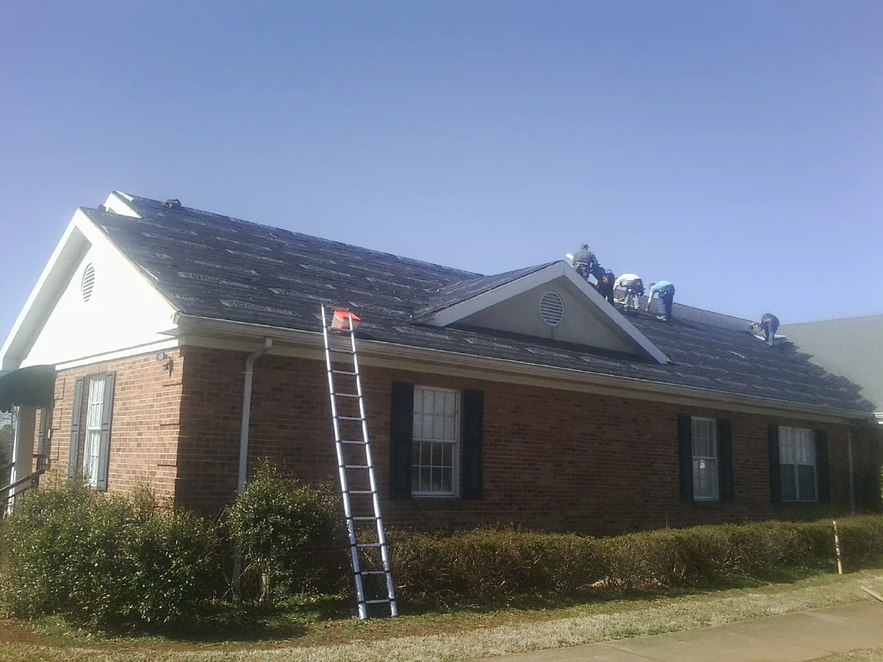 Crew tearing shingles off a brick ranch roof with a ladder set — Metal Roof Repair work by our crew in Brooker