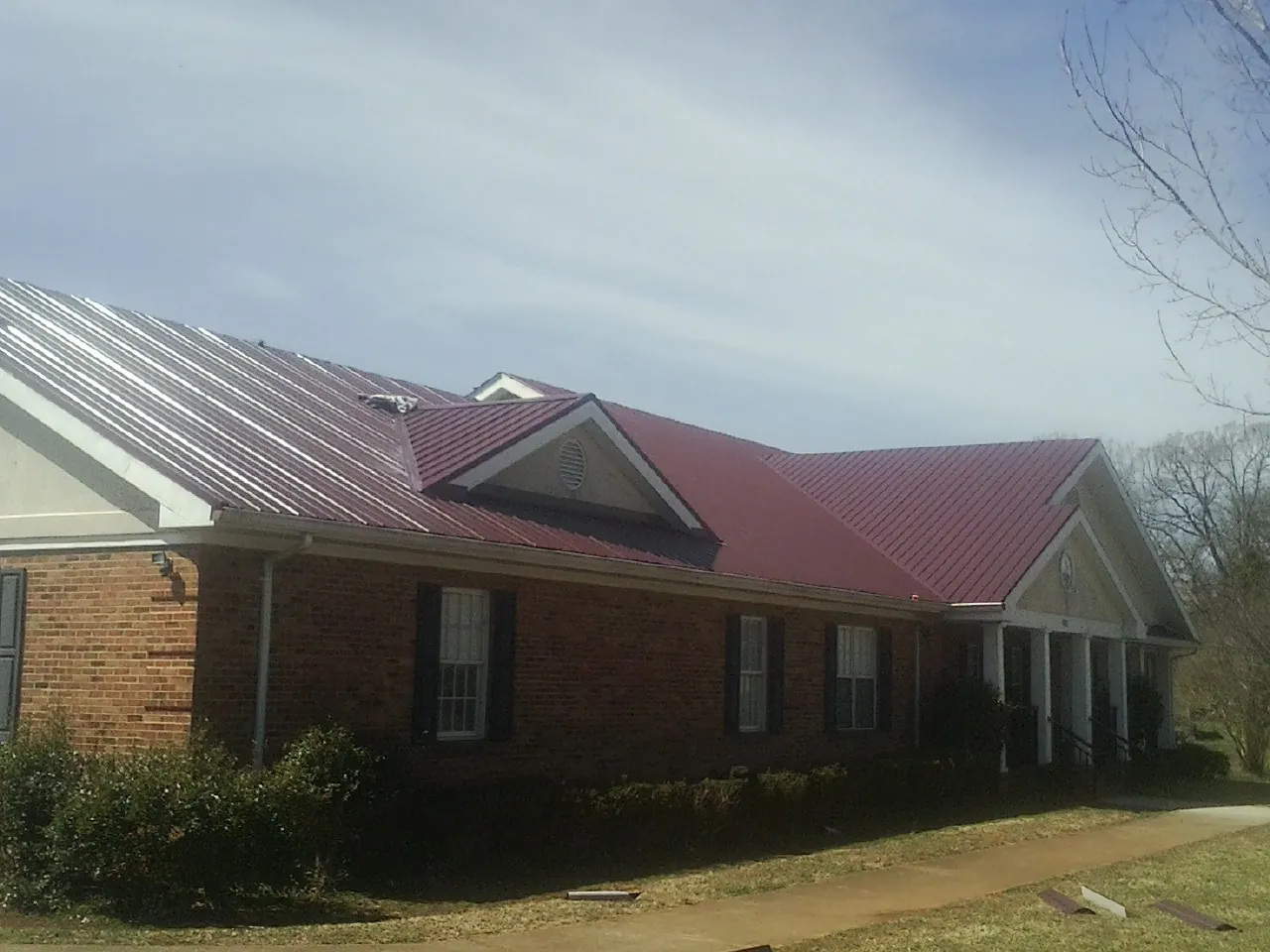 Red metal roof with gabled entries on a long brick building, from a Hail Damage Roof Repair job in Brooker