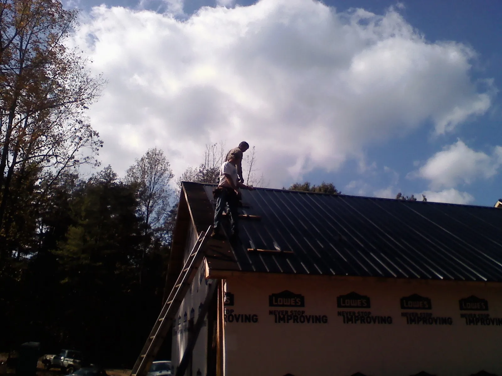 Roofer fastening dark metal panels high against a cloudy sky, from a Roof Inspection job in Brooker