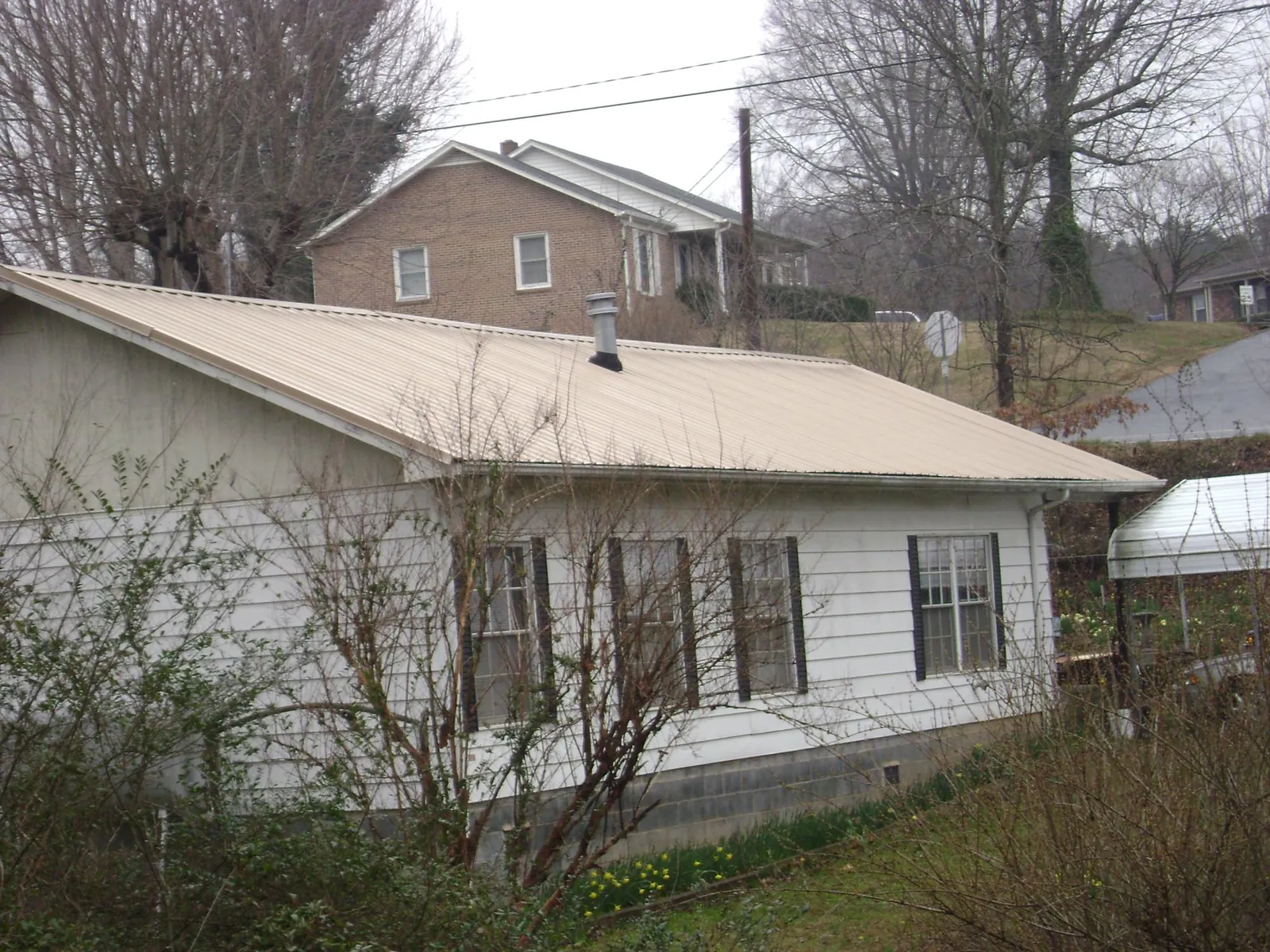 Tan metal roof on a white sided house set into a hillside — Commercial Roofing by Roofing Brothers in Brooker